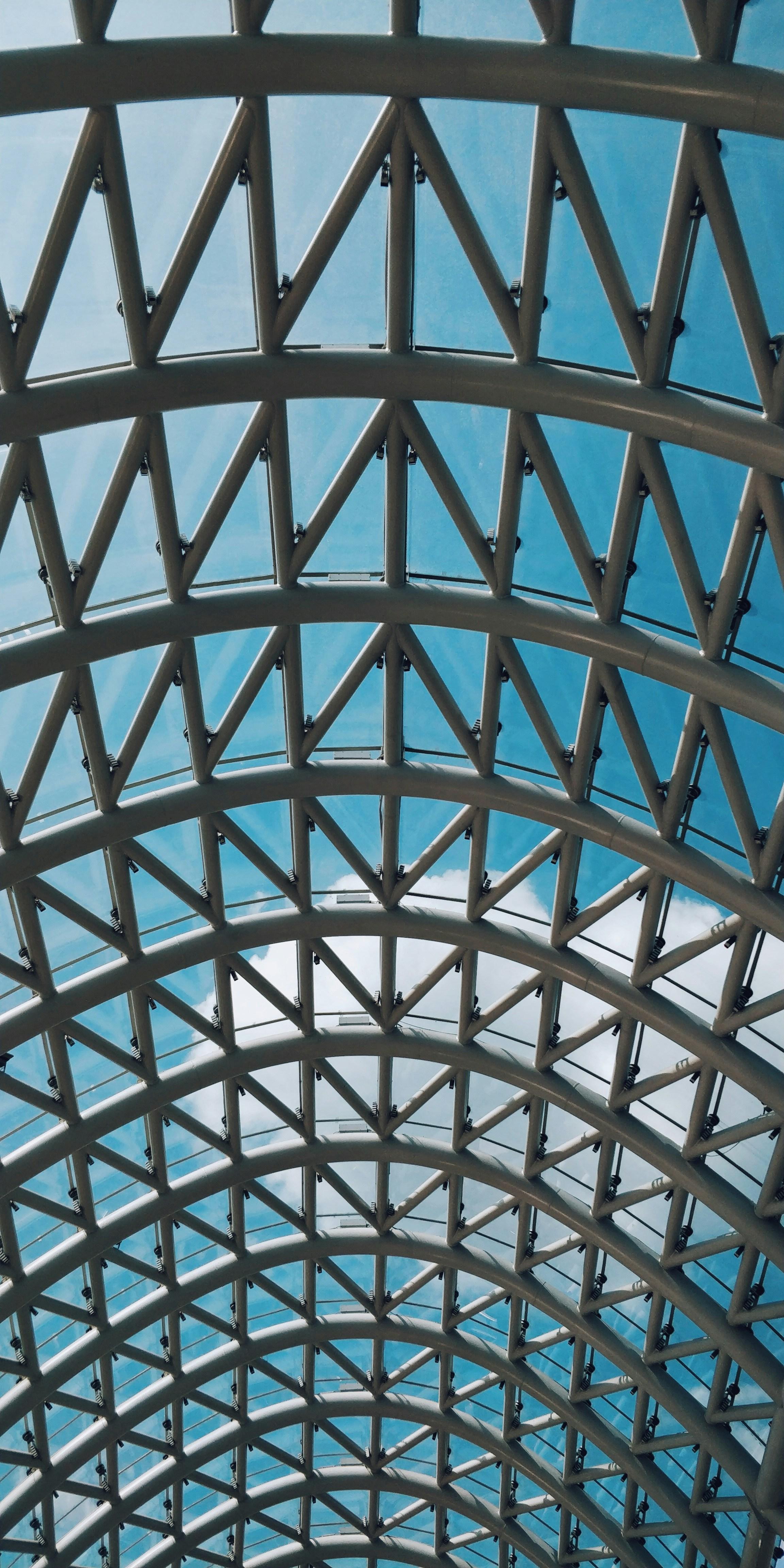 Geometric steel and glass roof structure beneath an open blue sky